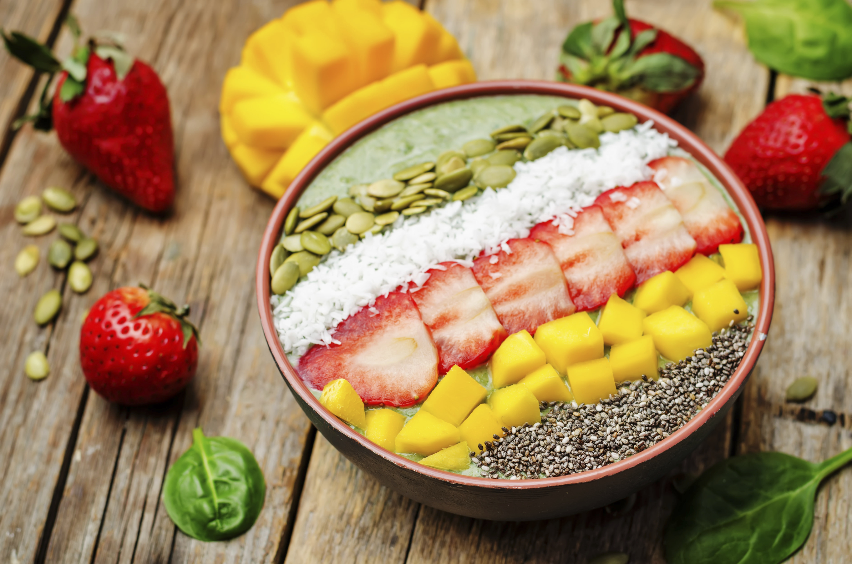 Spinach smoothie bowl with strawberries, coconut, mango, pumpkin seeds