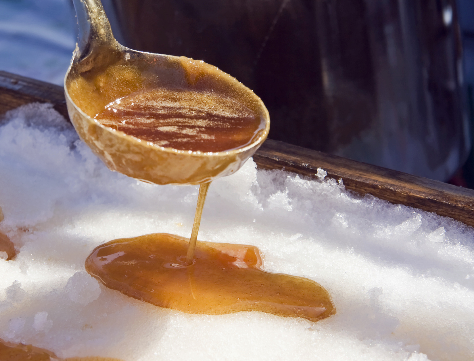 Pouring maple syrup from a ladle onto fresh snow