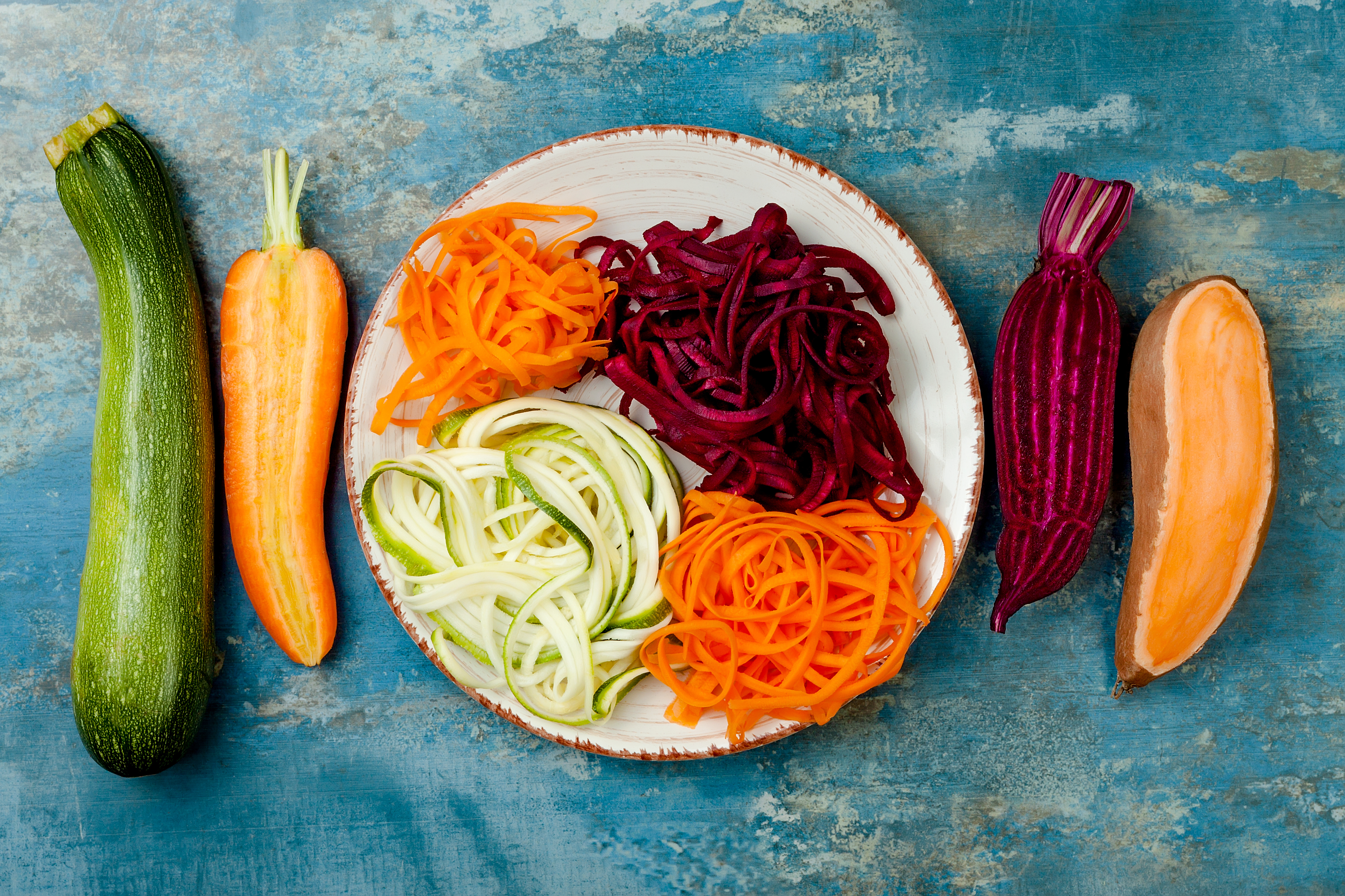 Zucchini, carrot, sweet potato and beetroot noodles on a plate. Top view, overhead, copy space. Blue rustic background
