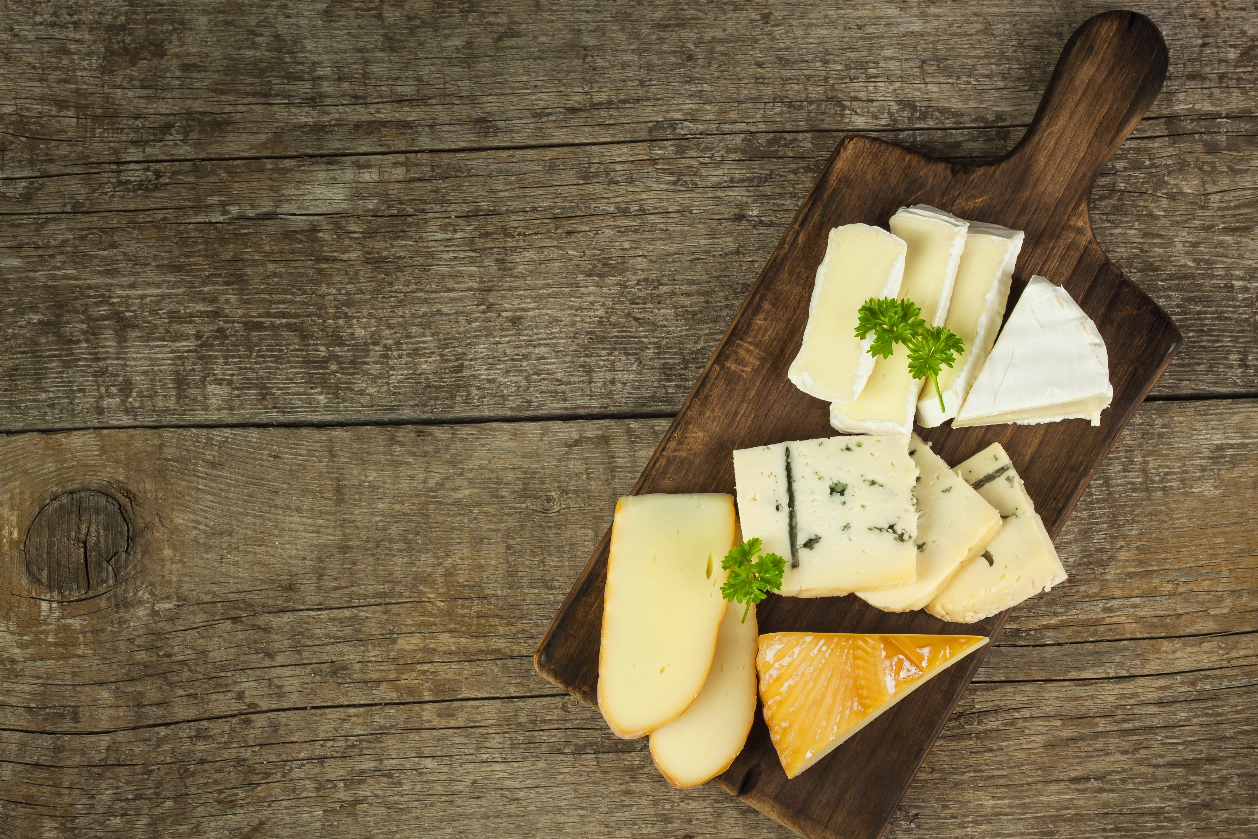 Different types of cheese on a wooden cutting board.