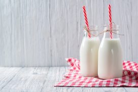 Bottles of milk with red straws and checkered towel on grey wooden background