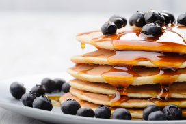 Plate of delicious pancakes close up, with fresh blueberries and maple syrup dripping