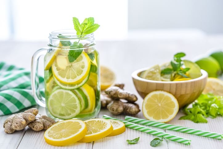 Front view of a mason jar filled with lemon and ginger infused water shot on white table. Some lemon slices, ginger roots and two green and white drinking straws complete the composition. Predominant colors are yellow, green and white. High resolution 42Mp studio digital capture taken with Sony A7rii and Sony FE 90mm f2.8 macro G OSS lens
