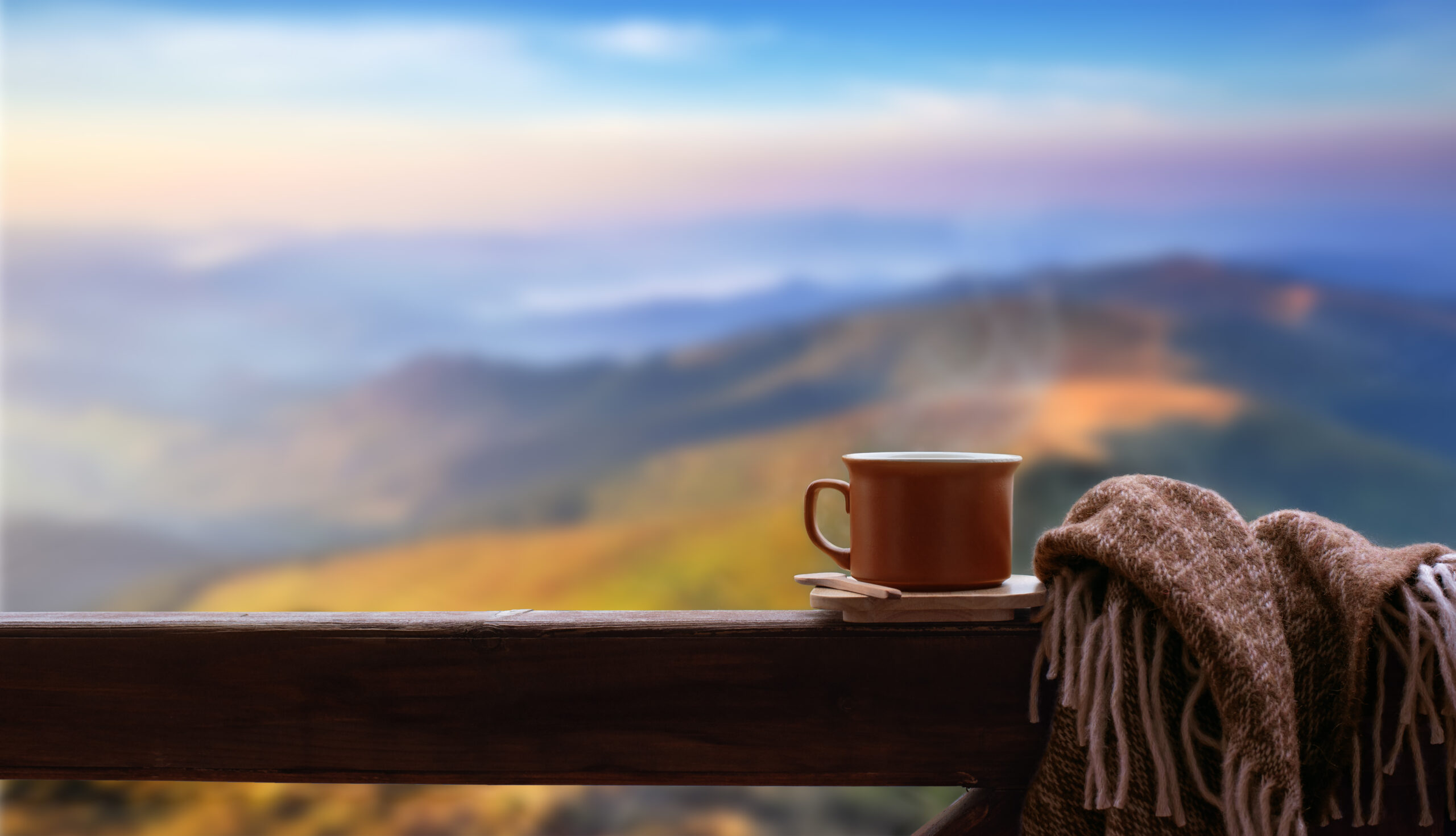 Hot cup of tea or coffee on the wooden railing on the mountains background.