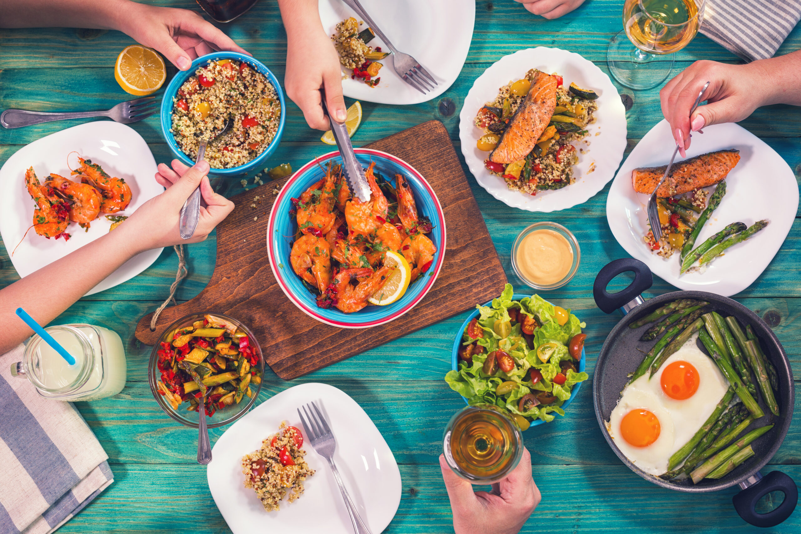 Young family having lunch at home. On the table are seafood,grilled salmon, couscous, grilled shrimp, asparagus with eggs and salad