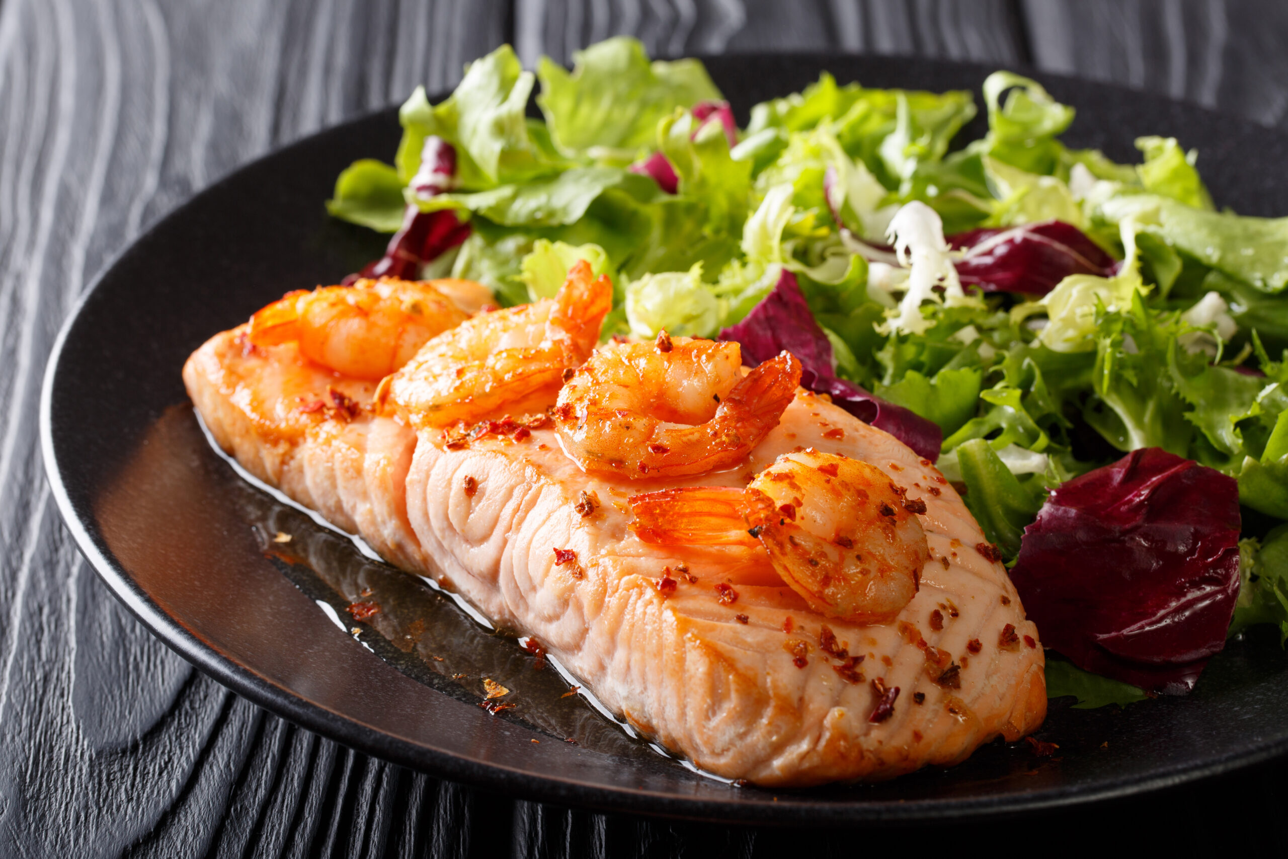 baked fillet of salmon with prawns and cayenne pepper and fresh salad on a plate close-up on a table. Horizontal