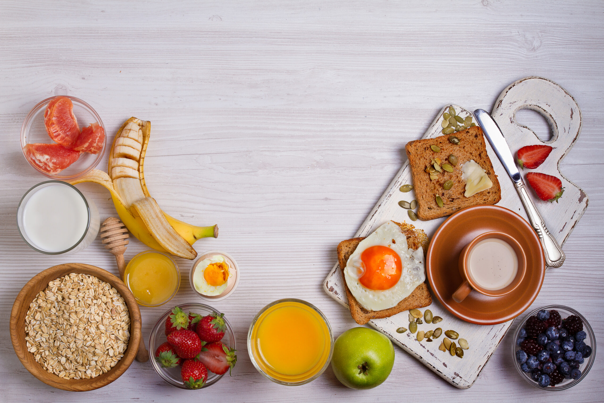 Breakfast served with coffee, orange juice, oat cereal, milk, fruits, eggs and toast. Balanced diet. Food background. View from above, top studio shot