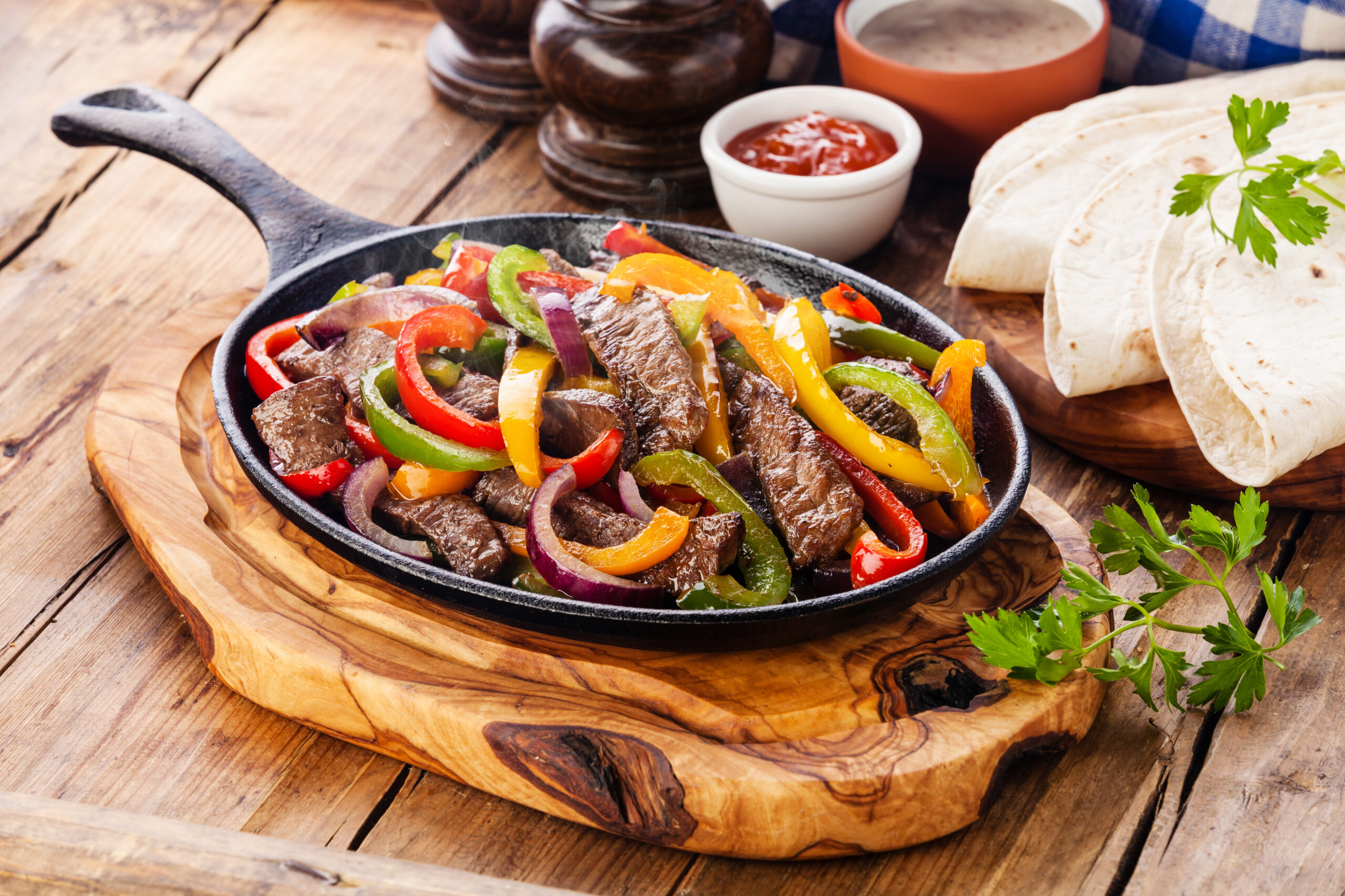 Beef Fajitas with colorful bell peppers in pan and tortilla bread and sauces