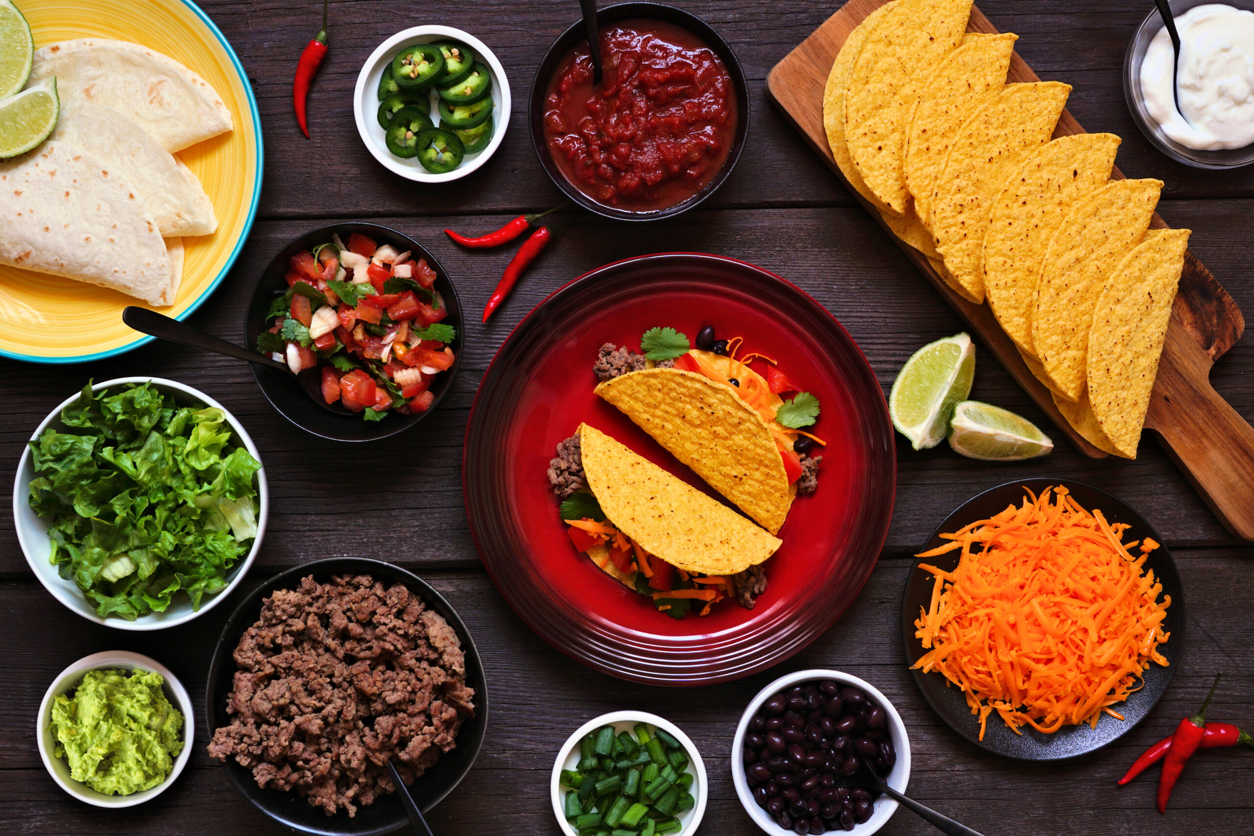 Taco bar table scene with a selection of ingredients. Above view on a dark wood background. Mexican food buffet.