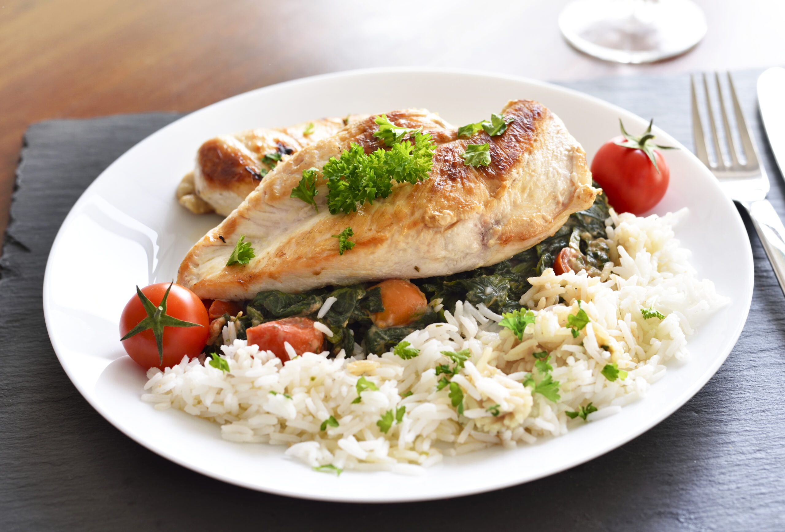 Grilled chicken breast with vegetables, rice and cherry tomatoes. Healthy eating scene, grilled chicken on a wooden table.