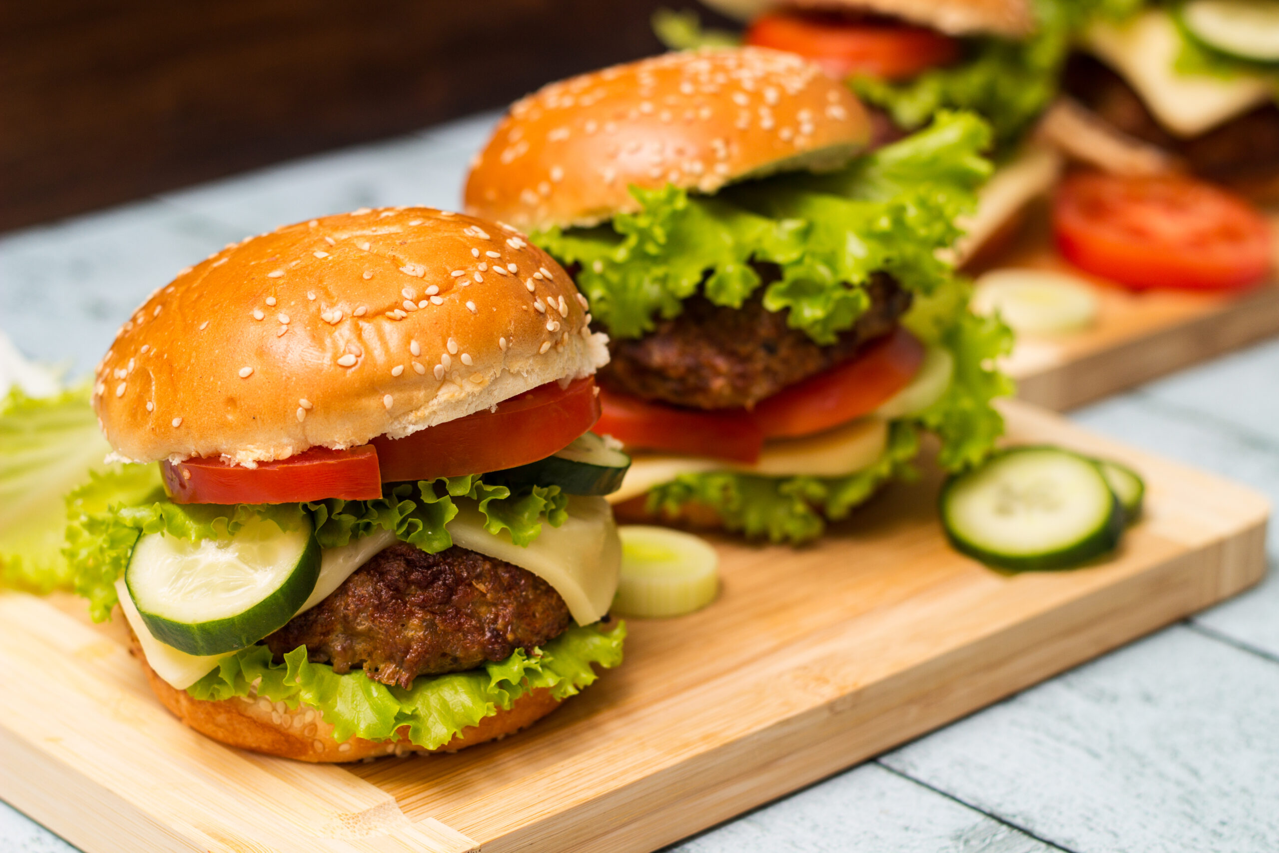 Burgers with beef meat, cheese and lettuce, served on cutting board