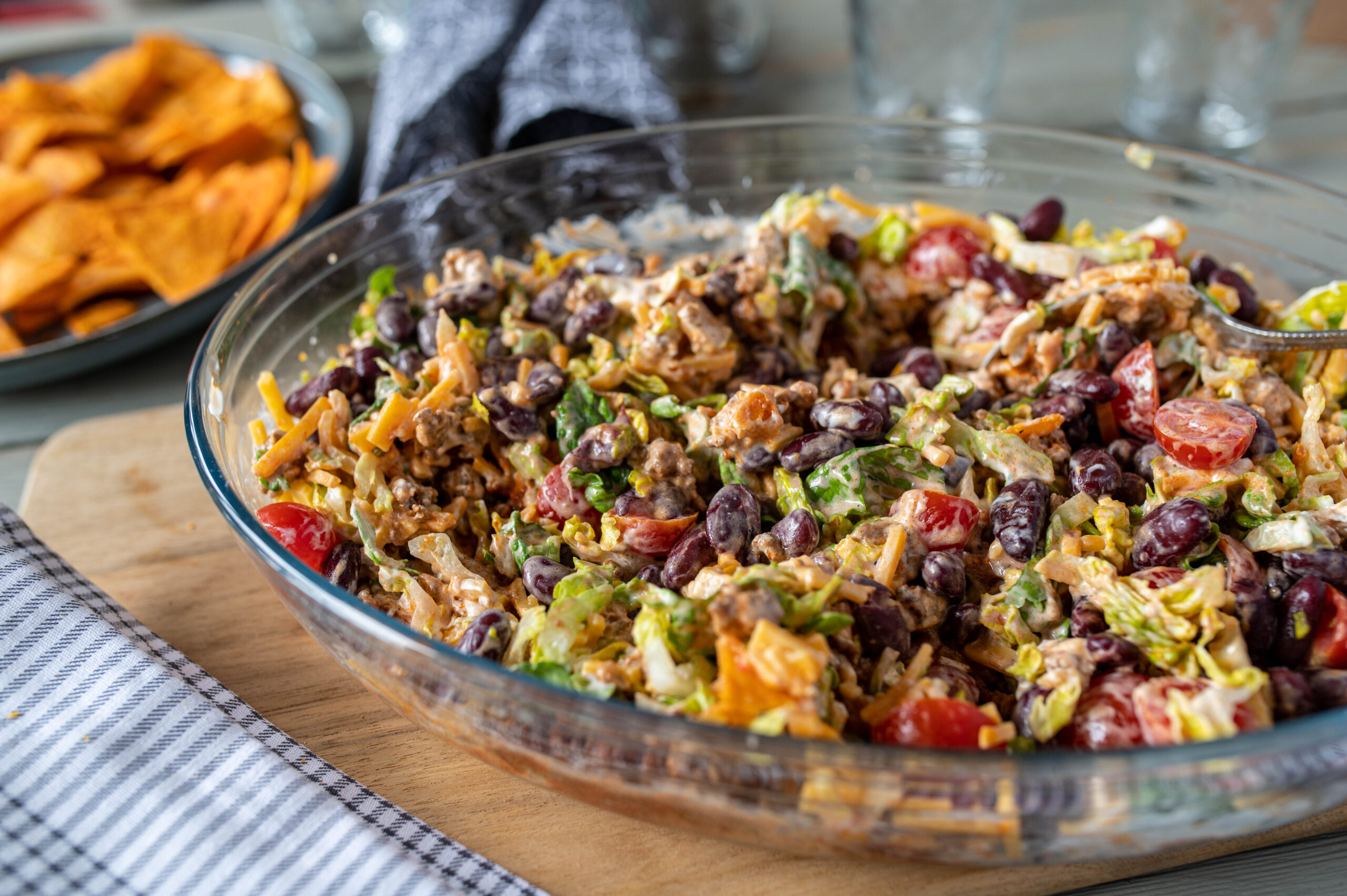 Delicious tex mex or mexican party food with a fresh and homemade taco salad with kidney beans, ground beef, cheddar cheese, romana salad, tomatoes and sour cream. Served mixed up in a large bowl on a table.