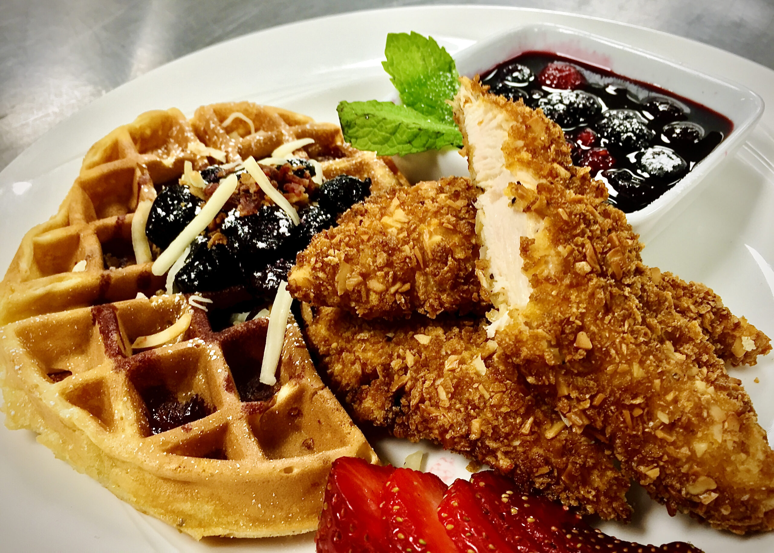Upscale buttermilk white cheddar cheese waffles fresh from the iron, served with almond and cornflake crusted chicken tenders.Served with dark cherry and blueberry compote