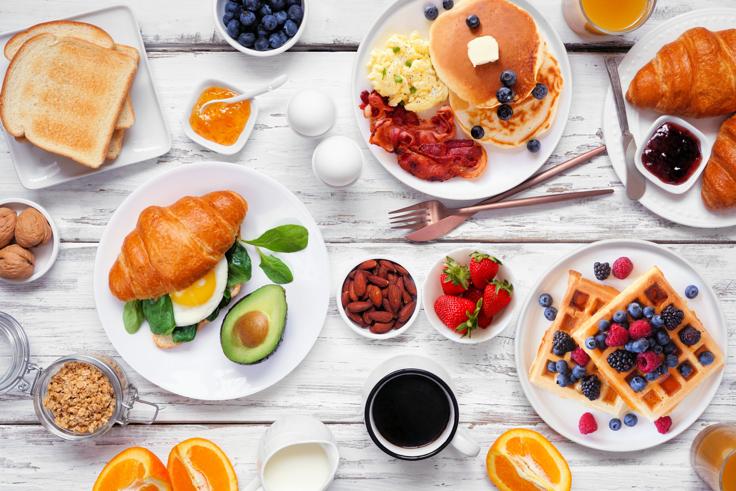 Breakfast or brunch table scene on a white wood background. Top view. Selection of sweet and savory food items.