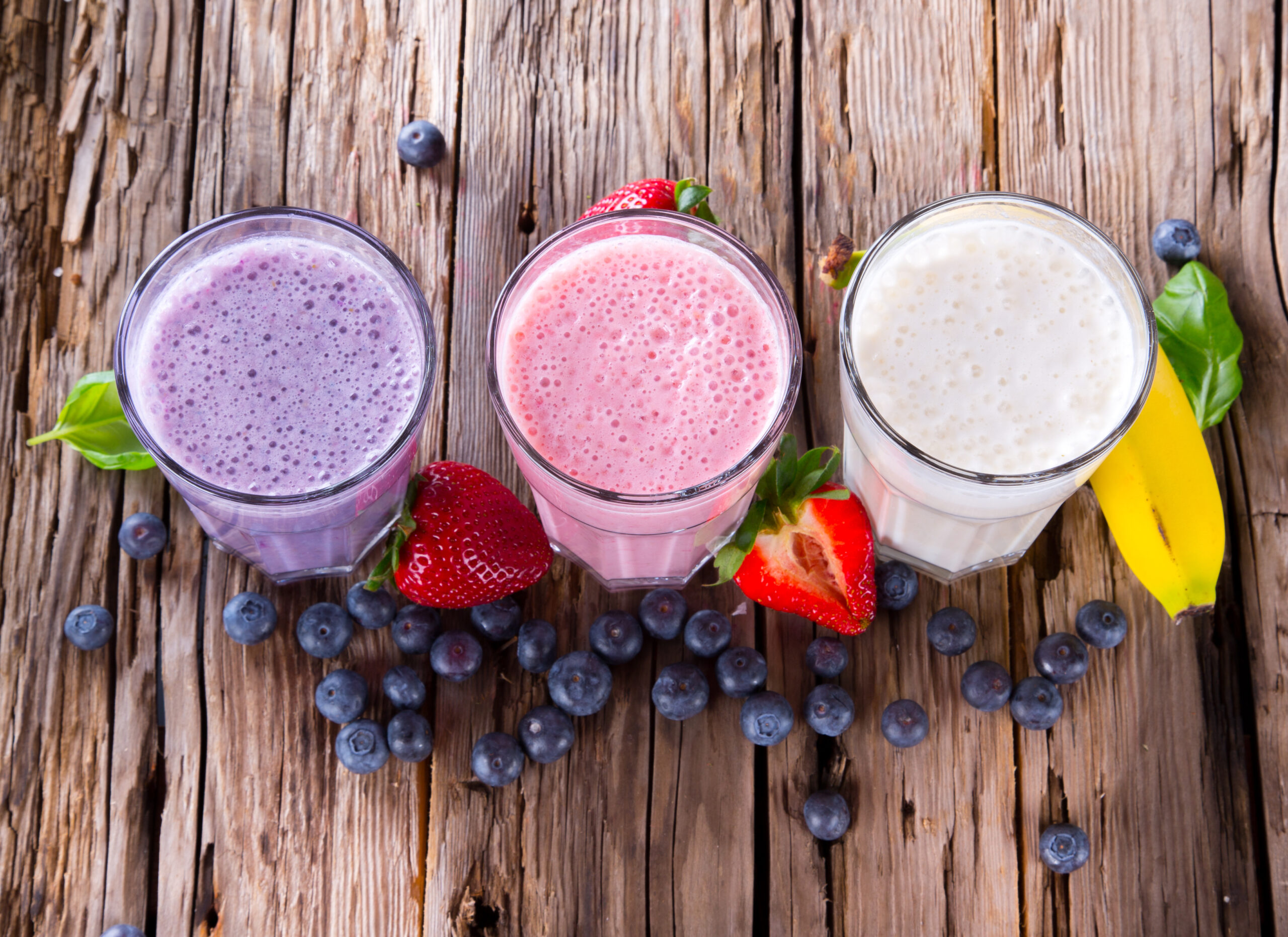 Fresh milk, strawberry, blueberry and banana drinks on wodeen table, assorted protein cocktails with fruits.