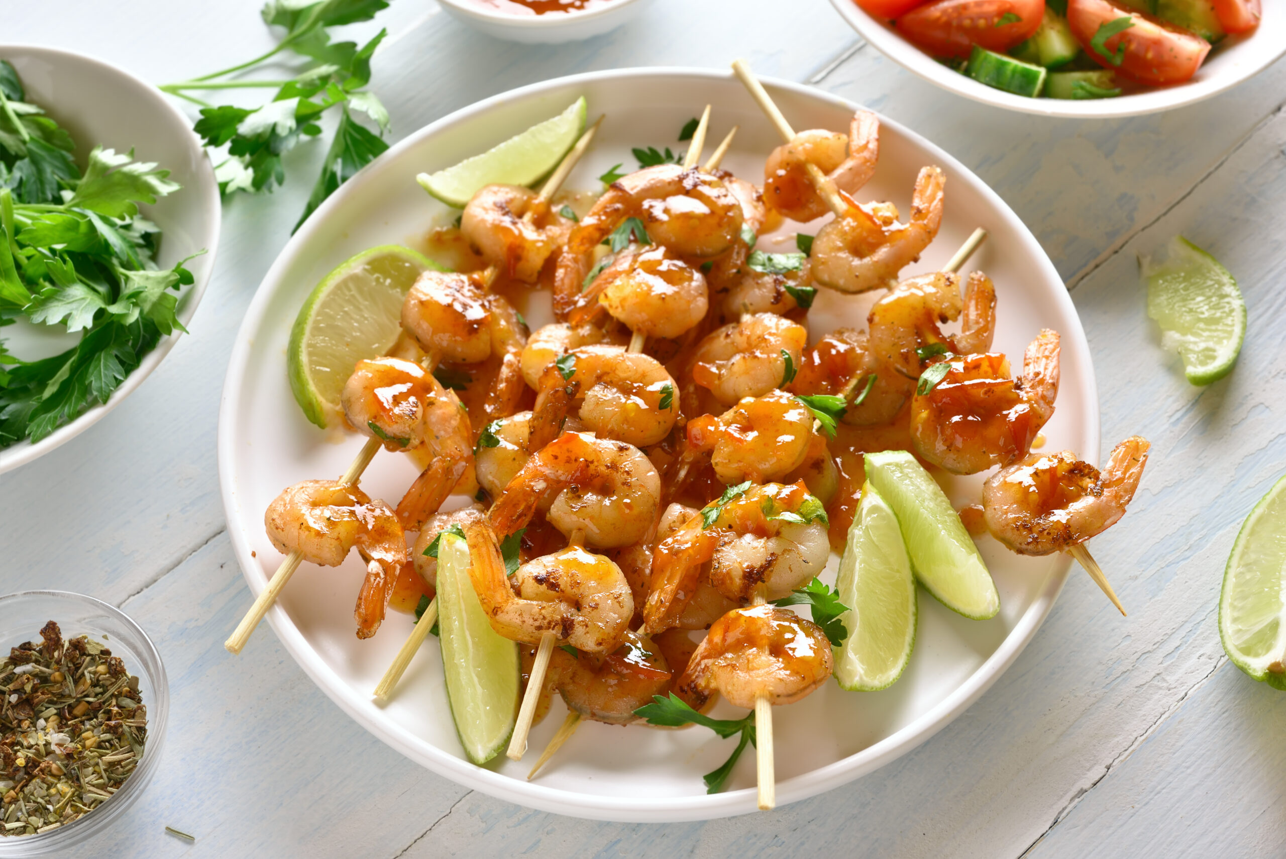 Prawns skewers Prawns skewers with greens, spices, lime and sauce on white plate over wooden table. Grilled shrimp skewers. Tasty seafood.