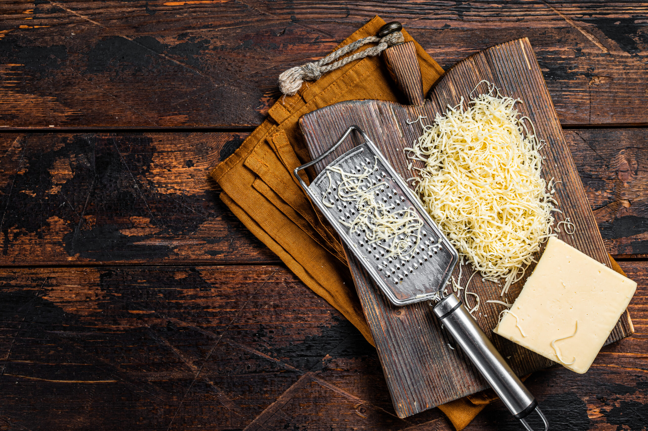 Piece of semi hard cheese and grated cheese with grater. Wooden background. Top view. copy space Piece of semi hard cheese and grated cheese with grater. Wooden background. Top view. copy space.