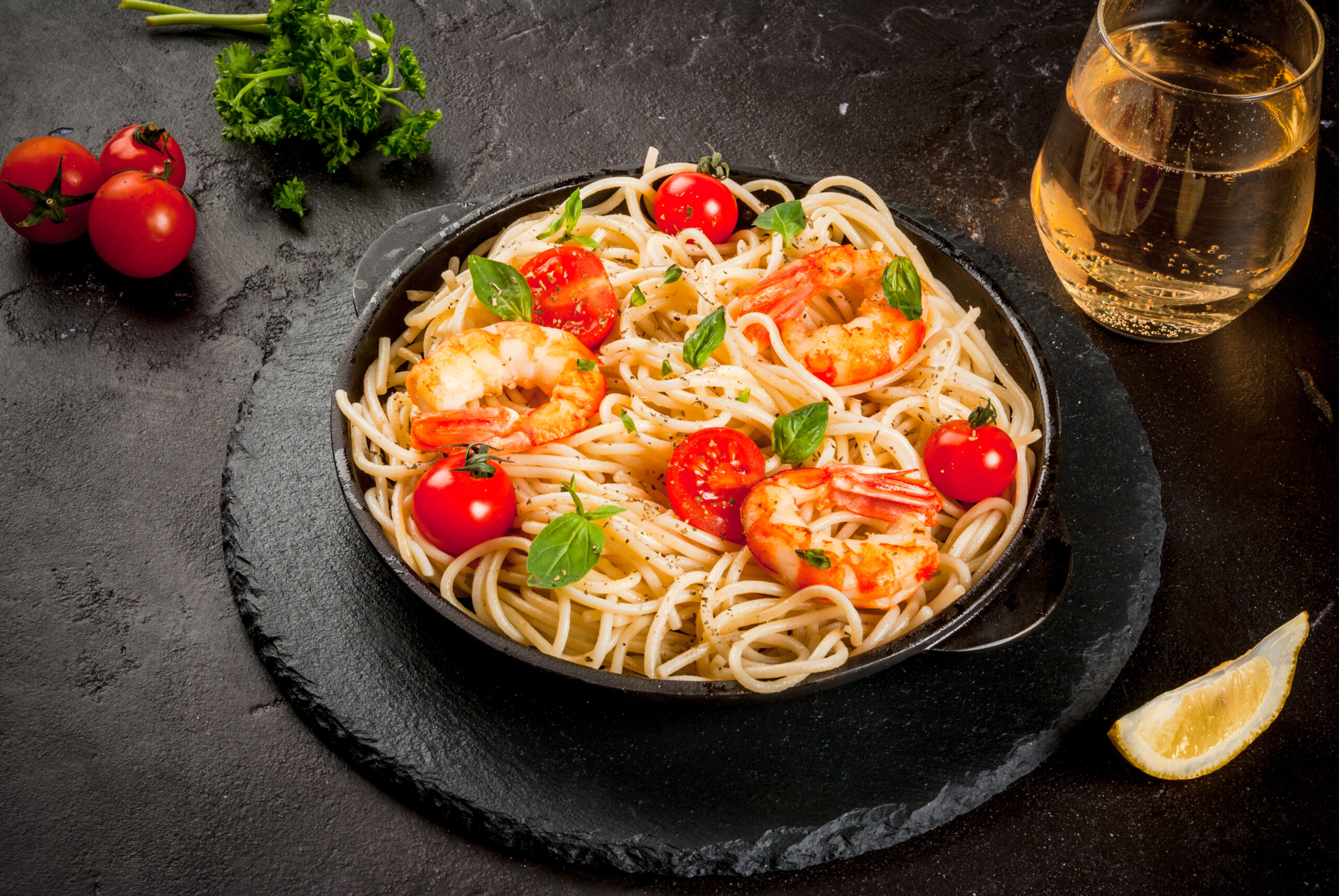 Pasta with grilled prawns shrimps Seafood. Shellfish. Pasta with grilled prawns shrimps, with tomatoes, fresh herbs (basil) and spices. On cast-iron frying pan, black concrete table, with glass of white wine, Copy space