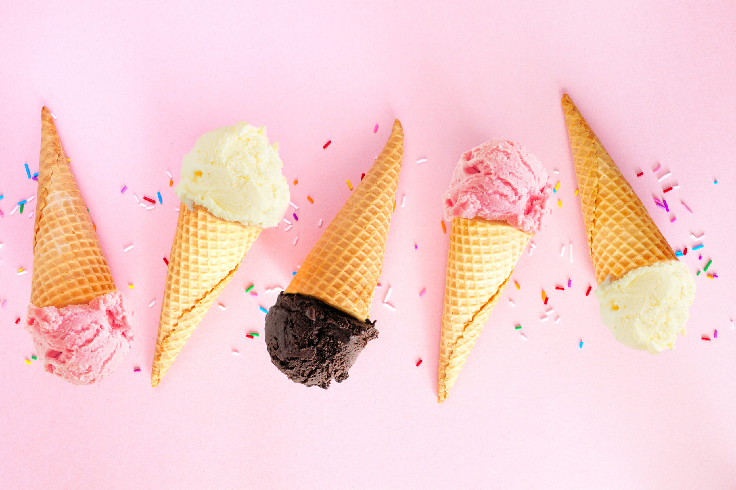 Ice cream cone flat lay over a pink background. Pink strawberry, white vanilla and dark chocolate flavors.