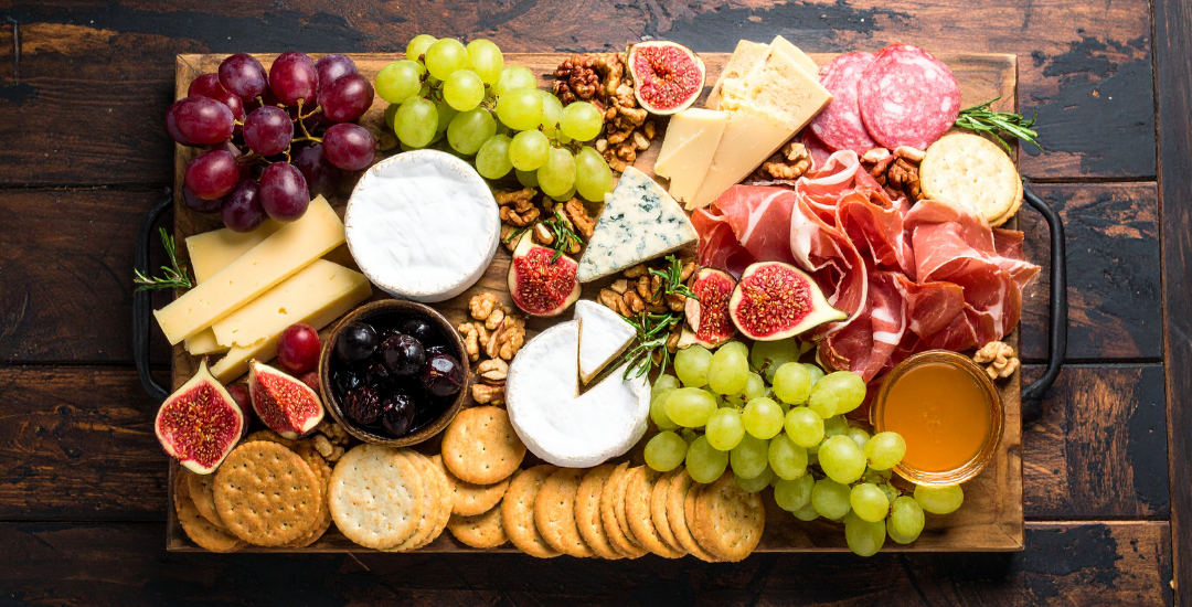 A Charcuterie Board full of meats, specialty cheeses, fresh fruit & crackers on a wood background