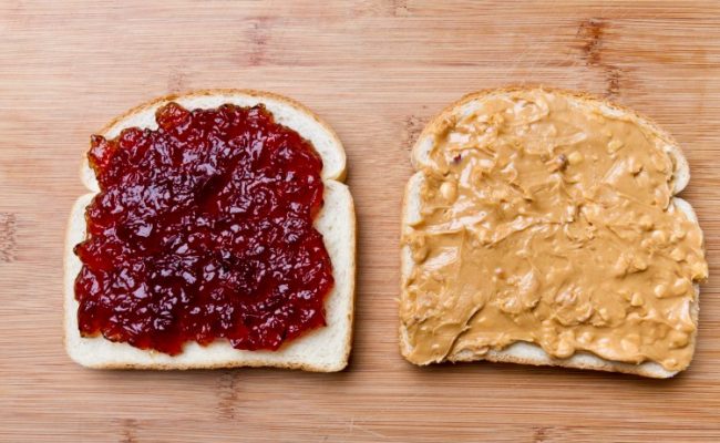 Open Face Peanut Butter and Jelly Sandwich Simple peanut butter and jelly sandwich with strawberry jam and chunky peanut butter on white bread, separated and placed on a bamboo cutting board with soft natural window light.